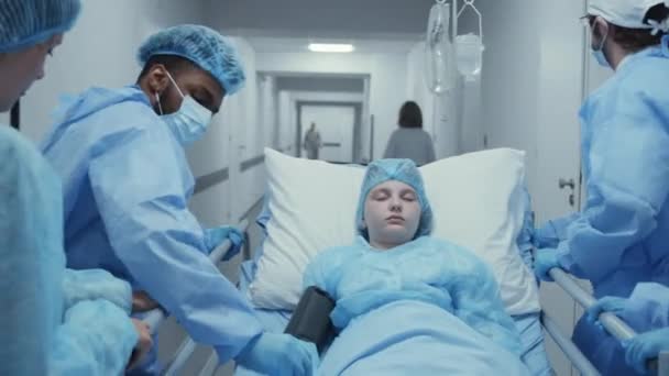 医生和孩子的妈妈带着生病的小女孩跑着把担架推进手术室 医生检查病人手上的脉搏血氧计 工作人员在应急部门工作 跟踪目标慢动作 — 图库视频影像