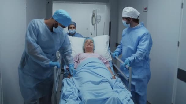 医生和医护人员把老年妇女推入骨科 与她交谈 医生检查病人手上的心率监测器 医护人员在急诊室工作 前面的景色跟踪射击 — 图库视频影像
