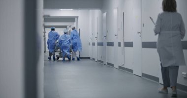 Doktorlar, hemşireler ve sağlık görevlileri hastayla birlikte sedyeyi ameliyathaneye götürün. Boyunluk takmış Afro-Amerikalı bir adam sedyede yatıyor. Acil serviste çok ırklı çalışanlar var. Ağır çekim. Arka plan.