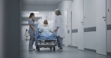 Olgun doktor ve hemşire yaralı bir hastayla klinik koridorunda yürüyor. Doktorlar sedyede yatan Afrikalı Amerikalı adamı hastane koğuşuna taşıyorlar. Tıp merkezinde çalışan tıbbi personel..