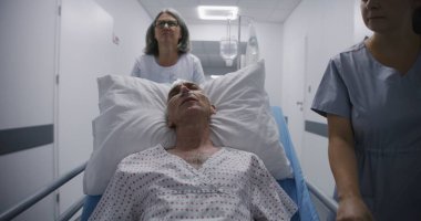 Eski hasta ameliyattan sonra tüp yutturulmuş bir şekilde sedyede uyuyor. Doktor ve hemşire yaşlı adamı klinik koridorunun aşağısındaki hastane koğuşuna naklediyor. Tıp merkezinde çalışan tıbbi personel..