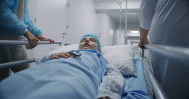 Genç hasta sedyede yatıyor, parmağında kan damlası ve nabız oksimetresi var. Profesyonel doktorlar ve anne nakil kızı ameliyathaneye. Anne kızının elini tutuyor. Klinikte çalışan tıbbi personel.