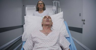 Eski hasta ameliyattan sonra tüp yutturulmuş bir şekilde sedyede uyuyor. Doktor ve hemşire yaşlı adamı klinik koridorunun aşağısındaki hastane koğuşuna naklediyor. Tıp merkezinde çalışan tıbbi personel..
