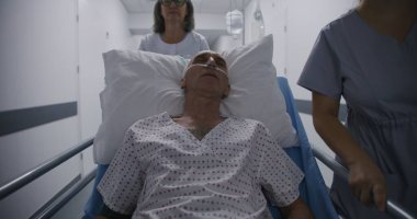 Eski hasta ameliyattan sonra tüp yutturulmuş bir şekilde sedyede uyuyor. Doktor ve hemşire yaşlı adamı klinik koridorunun aşağısındaki hastane koğuşuna naklediyor. Tıp merkezinde çalışan tıbbi personel..