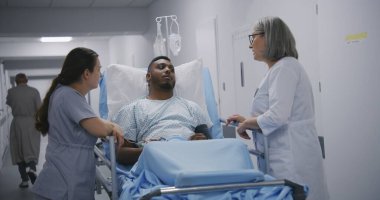 Ameliyattan önce sedye üzerinde yatan Afrikalı Amerikalı bir kadın doktor. Hemşire ve hekim hasta koridorunda sedyenin yanında duruyor. Acil serviste tıbbi personel işi..