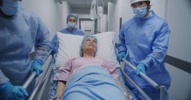 Doktorlar ve sağlık görevlileri yaşlı kadınla sedyeyi itin ve onunla konuşun. Doktor hasta elinin nabzını kontrol ediyor. Sağlık personeli acil serviste çalışıyor. Ön manzara. İzleme görüntüsü.
