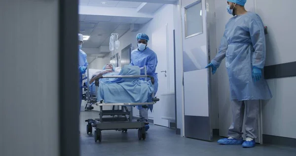 看護師と救急隊員はすぐに医療施設の廊下ドアを開けました 複数のエスニック外科医が重傷を負った高齢男性を手術室に押し込む 救急部に勤務する医療スタッフ — ストック写真
