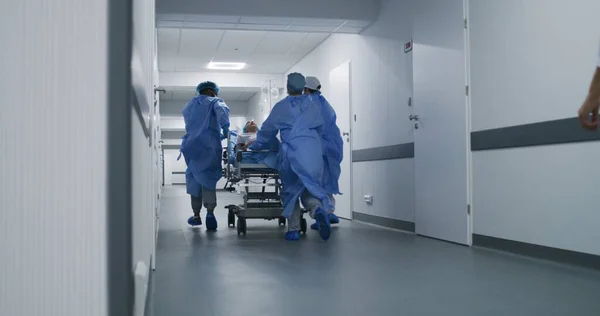 Doctors, nurses and paramedics run and push stretcher with seriously injured patient to surgery room. Medical personnel save human life in emergency department. Medical facility hallway. Slow motion.