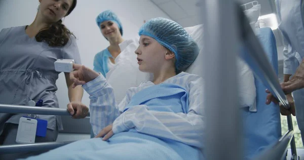 女孩躺在格尔内 与护士和母亲交谈 并向医生显示脉搏血氧计 医生和护士将年轻病人运送到医院门廊下病房 工作的医务人员 — 图库照片
