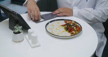 Profesyonel doktor klinikteki kafede oturur ve dijital tablet bilgisayardaki test sonuçlarını inceler. Kafeterya çalışanı sıhhiyeye yemek getiriyor. Sağlık personeli hastane veya tıp merkezi kantininde yemek yer..