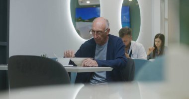 Kıdemli hasta hastane kafeteryasında oturur, yemek yer ve doktorların izinleriyle konuşur. Yetişkin doktor arka planda yemek yiyor. Tıbbi personel ve hastalar tıp merkezi kantininde dinleniyor..