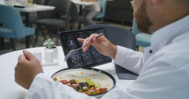 Profesyonel doktor, klinikteki kafede dijital tablet kullanarak MRI veya CT taramasını izliyor. Sıhhiye yemeğini yer, hastanın beyin tarama sonuçlarını inceler. Sağlık personeli hastane kantininde yemek yiyor..