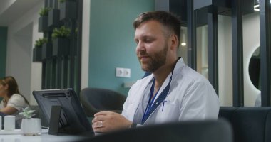 Profesyonel doktor hastasının test sonuçlarını dijital tablet bilgisayarda izler ve kahve içer. Kadın doktor arka plandaki kadınla konuşuyor. Modern hastane kantininde çalışan tıbbi personel.