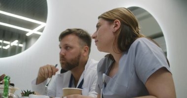 Erkek doktor ve hemşire modern klinik kafesinde oturuyor. Profesyonel doktorlar yemek yer, yemekte sohbet eder, iş tartışır. Hastane ya da tıp merkezi kafeteryasında tıbbi personel. Yaşam tarzı ve sağlık hizmeti kavramı.