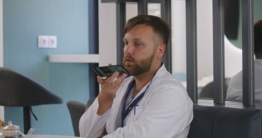 Erkek doktor molada klinikteki kafede oturuyor. Sağlık uzmanı telefonla konuşuyor, sosyal ağ ya da mesajlaşma uygulaması kullanarak sesli mesaj kaydediyor. Hastane veya Tıp Merkezi yemek odasında tıbbi personel.