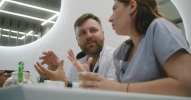 Erkek doktor ve hemşire modern klinik kafesinde oturuyor. Profesyonel doktorlar yemek yer, yemekte sohbet eder, iş tartışır. Hastane ya da tıp merkezi kafeteryasında tıbbi personel. Yaşam tarzı ve sağlık hizmeti kavramı.