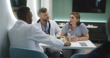 Afrikalı Amerikalı doktor klinikteki kafede iş arkadaşlarıyla oturuyor. Profesyonel sıhhiyeciler yemek boyunca konuşur. MRI beyin taraması görüntülü dijital tablet. Hastane veya tıp merkezi kafeteryasında tıbbi personel.