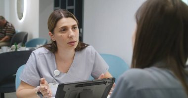 Kadın doktor, klinikteki kafede hastayla görüşüyor, dijital tablet bilgisayar kullanıyor. Profesyonel doktor kadınlarla konuşur, tıbbi testlerin sonuçlarını tartışır. Hastane ya da Tıp Merkezi Kafeteryası.