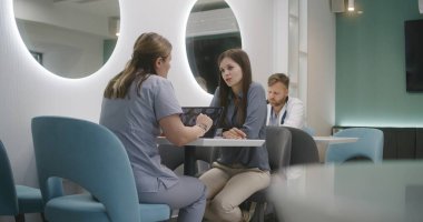 Kadın doktor, klinikteki kafede hastasıyla oturuyor. Profesyonel sıhhiyeci kadınlarla tıbbi teşhis sonuçlarını tartışıyor. MRI veya CT görüntülü dijital tablet. Hastane ya da Tıp Merkezi Kafeteryası.