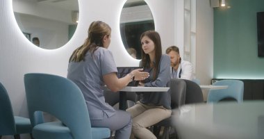 Kadın doktor, klinikteki kafede hastasıyla oturuyor. Profesyonel sıhhiyeci kadınlarla tıbbi teşhis sonuçlarını tartışıyor. MRI veya CT görüntülü dijital tablet. Hastane ya da Tıp Merkezi Kafeteryası.