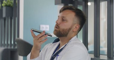 Erkek doktor klinikteki kafede oturuyor. Profesyonel doktorların telefonla konuşmalarını kapat, sosyal ağ ya da mesajlaşma uygulaması kullanarak sesli mesaj kaydet. Hastane veya tıp merkezi kafeteryasında tıbbi personel.