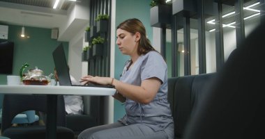 Kadın doktor klinikte oturuyor, dizüstü bilgisayar kullanıyor. Sağlık uzmanları hastalarla çevrimiçi iletişim kuruyor, tıbbi testlerin sonuçlarını inceliyor ya da internette sörf yapıyor. Hastane kafeteryasında çalışan tıbbi personel..