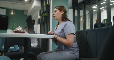 Kadın doktor klinikte oturuyor, dizüstü bilgisayar kullanıyor. Profesyonel sağlık danışmanları ve hastalarla görüntülü sohbet yoluyla görüşmeler, çevrimiçi danışmanlık hizmeti sunuyor. Hastane veya Tıp Merkezi yemek odasında tıbbi personel.