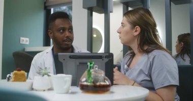 Klinikte çok ırklı doktorlar oturuyor. Profesyonel doktorlar konuşur, tıbbi testlerin sonuçlarını dijital tablet kullanarak inceler, teşhisi tartışırlar. Hastane veya tıp merkezi kafeteryasında çalışan tıbbi personel.