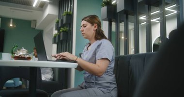Kadın doktor klinikte oturuyor, dizüstü bilgisayar kullanıyor. Sağlık uzmanları hastalarla çevrimiçi iletişim kuruyor, tıbbi testlerin sonuçlarını inceliyor ya da internette sörf yapıyor. Hastane kafeteryasında çalışan tıbbi personel..