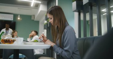 Kadın klinikteki masada oturuyor, telefon kullanıyor. Kafeterya çalışanı kadın ziyaretçiye yemek getiriyor. Tıp personeli, doktorlar ve hastalar modern tıp merkezinde veya hastane yemek odasında yemek yerler..