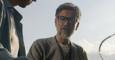 Yetişkin bir doktorun hastasıyla bankta oturup muayene ettiği yakın çekim. Orta yaşlı bir adam sağlık uzmanına ağrıdan şikayetçi. Sıhhiye müşteriye danışıyor ve tedavisini dışarıda tartışıyor.