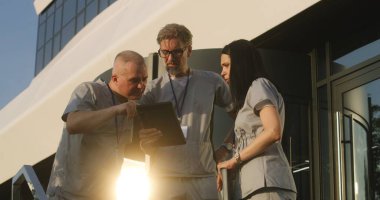 Üniformalı doktorlar hastane girişinde bekliyor. Profesyonel doktorlar hastaların teşhislerini tartışıyor, dijital tablet kullanıyorlar. Modern kliniğin ya da tıp merkezinin tıbbi personeli. Sağlık hizmetleri sistemi.