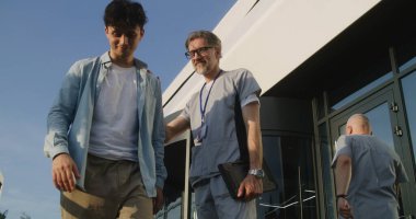 Elinde tabletle yetişkin bir doktor kliniğin girişinde hastayla duruyor ve tedaviyi tartışıyor. Sağlık uzmanı randevudan sonra müşteriye veda ediyor, sonra da kameraya bakıyor. Sıhhiye dışarıda çalışıyor..