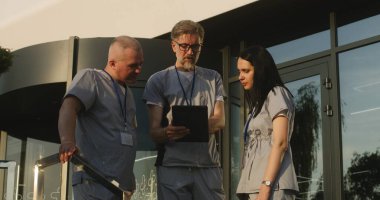Üniformalı doktorlar hastane girişinde bekliyor. Profesyonel doktorlar hastaların teşhislerini tartışıyor, dijital tablet kullanıyorlar. Modern kliniğin ya da tıp merkezinin tıbbi personeli. Sağlık hizmetleri sistemi.