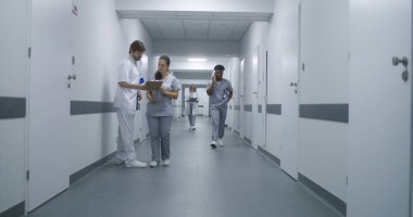 Üniformalı klinik koridorunda çok ırklı tıbbi personel var. Yaşlı hasta doktorla randevuya gider. Sağlık uzmanları sağlık merkezi koridorunda karşılıyorlar..