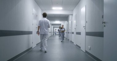 Üniformalı klinik koridorunda çok ırklı tıbbi personel var. Yaşlı hasta doktorla randevuya gider. Sağlık uzmanları sağlık merkezi koridorunda karşılıyorlar..