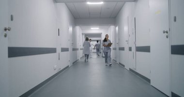 Üniformalı klinik koridorunda çok ırklı tıbbi personel var. Yaşlı hasta doktorla randevuya gider. Sağlık uzmanları sağlık merkezi koridorunda karşılıyorlar. Dolly vurdu. Arka plan.
