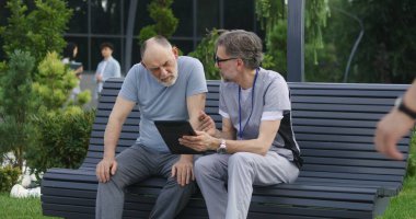 Elinde tabletle yetişkin bir doktor yaşlı bir hastasıyla bankta oturur ve ona danışır. Üniformalı doktor, dijital tablet bilgisayar kullanarak müşterilerine ilaç yazıyor. Sağlık personeli dışarıda çalışıyor..