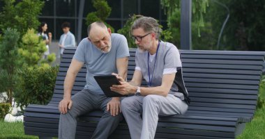 Elinde tabletle yetişkin bir doktor yaşlı bir hastasıyla bankta oturur ve ona danışır. Üniformalı doktor, dijital tablet bilgisayar kullanarak müşterilerine ilaç yazıyor. Sağlık personeli dışarıda çalışıyor..