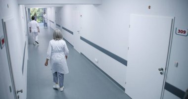 Parlak klinik koridoru: Meşgul doktorlar, profesyonel sağlık görevlileri, hemşireler, doktorlar ve çeşitli hastalar yürüyor. Tıp personeli modern hastane ya da tıp merkezinde çalışıyor. Güvenlik kamerası görüntüsü. Yüksek açı.