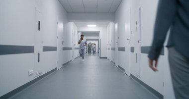 Kadın tıp merkezi koridoruna gider, Afrikalı Amerikalı doktorla konuşur. Hemşire ve yaşlı hasta klinik koridorunda yürür, test sonuçlarını tartışırlar. Klinikte çok ırklı tıbbi personel.
