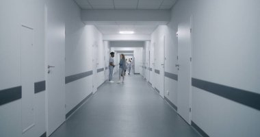 Kadın tıp merkezi koridoruna gider, Afrikalı Amerikalı doktorla konuşur. Hemşire ve yaşlı hasta klinik koridorunda yürür, test sonuçlarını tartışırlar. Klinikte çok ırklı tıbbi personel.