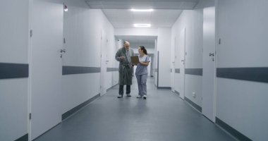 Üniformalı klinik koridorunda çok ırklı tıbbi personel var. Yaşlı hasta doktorla randevuya gider. Sağlık uzmanları sağlık merkezi koridorunda karşılıyorlar..