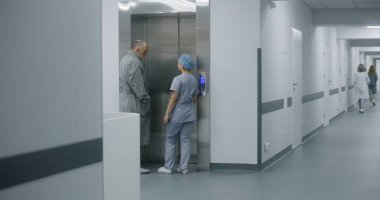Üniformalı hemşire yaşlı adamla hastane koridorunda yürür ve asansör kapısına gelir. Kadın sağlık uzmanı yaşlı bir hastayla tıp merkezi koridorunda buluşuyor. Modern klinikte tıbbi personel çalışması.