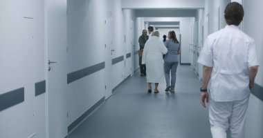Dijital tabletli kadın doktor, yaşlı bir kadınla klinik koridorunda yürüyen hemşire, hastaların prosedürlerden sonra hastane koğuşuna gitmesine yardım ediyor. Sağlık personeli, hastane koridorundaki hastalar..