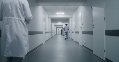 Üniformalı klinik koridorunda çok ırklı tıbbi personel var. Yaşlı hasta doktorla randevuya gider. Sağlık uzmanları sağlık merkezi koridorunda karşılıyorlar..