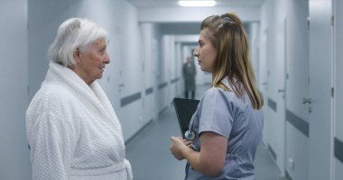 Kadın doktor, dijital tabletli hemşire ve hasta sohbeti. Doktor, prosedürlerden sonra yaşlı bir kadınla modern klinik koridorunda duruyor. Hastane ya da tıp merkezi koridorundaki hasta ve sağlık personeli.