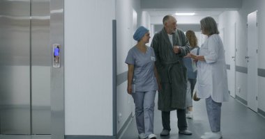 Hemşire ve kıdemli hasta asansöre gidip haber verin. Yaşlı hasta hastane koridorunda yetişkin doktorla konuşuyor. Afrikalı Amerikalı doktor koridorda tekerlekli sandalyeyle yürüyor. Tıbbi personel iş başında..