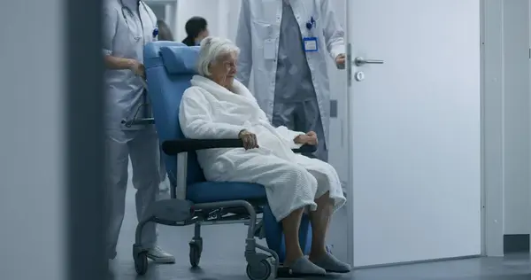 医師は 車椅子の手術室や手術室から高齢の女性を連れ出します 高齢者は病院の部屋に廊下を歩いている クリニックや医療センターの廊下の医療スタッフと患者 — ストック写真