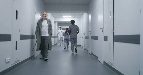 身穿制服的多种族医护人员步行诊所走廊 老年病人去看医生 医护专家在医疗中心走廊向您致意 — 图库照片